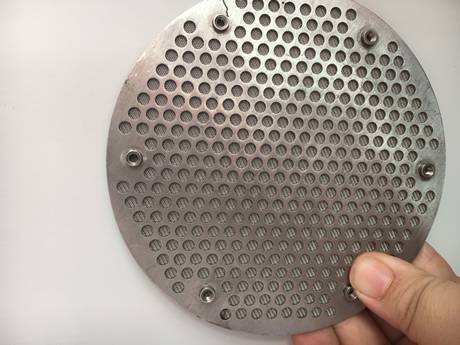 Uma mão está guardando uma forma redonda perfurou o disco aglomerado metal do filtro.